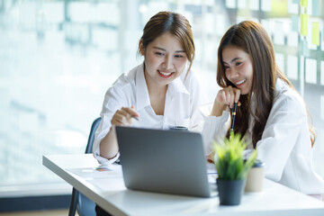 Two excited young girls or Asian businesswoman show joyful expressions of success at work smiling happily with a laptop computer in a modern office.