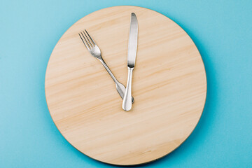 The concept of intermittent fasting and skipping meals. Wooden round tray with cutlery in the form of clock hands