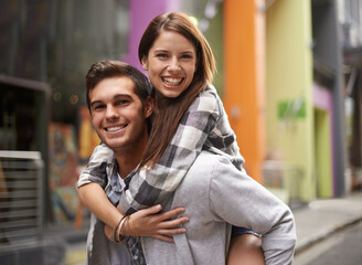 Totally in love. A young guy smiling while piggybacking his girlfriend out in the street.