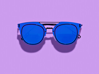Fashionable retro shape sunglasses with blue lenses placed on purple background. Minimalist background. Trendy colour of spring summer season. Eyes protection concept.