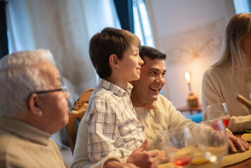Fototapeta na wymiar Happy father and his son laughing during family dinner. Multigenerational family sitting at table and having meal together. Family party concept