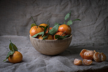 Closeup of the fresh sweet mandarins in the wooden bowl on a gray fabric