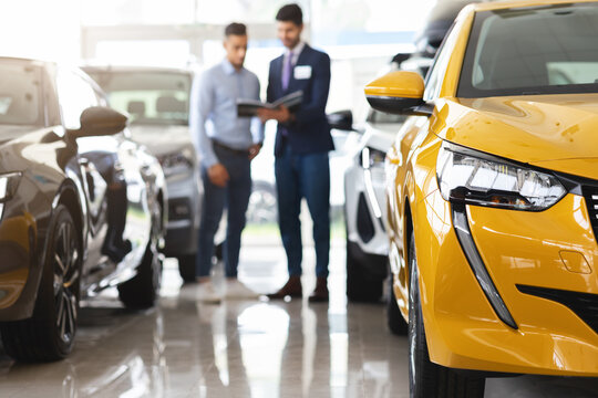Customer standing among cars, having conversation with sales assistant