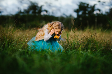 Blond girl child smells single orange lily