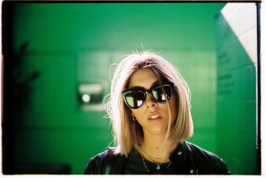 Blond woman on a green room with sunglasses and backlight