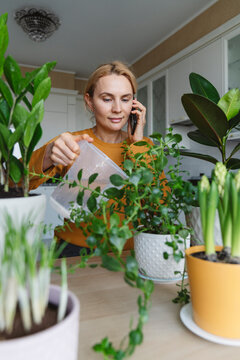 A nice woman waters indoor plants at home and talks on the phone.