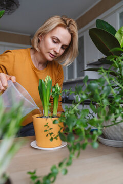 A nice woman in a yellow jacket is watering indoor plants.