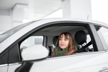 Portrait of a confident young woman sitting on the driver's seat of her white car at gas station. Caucasian woman wearing winter clothes