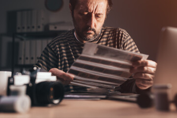 Photographer reviewing old analog camera 35 negative filmstrip at his workplace