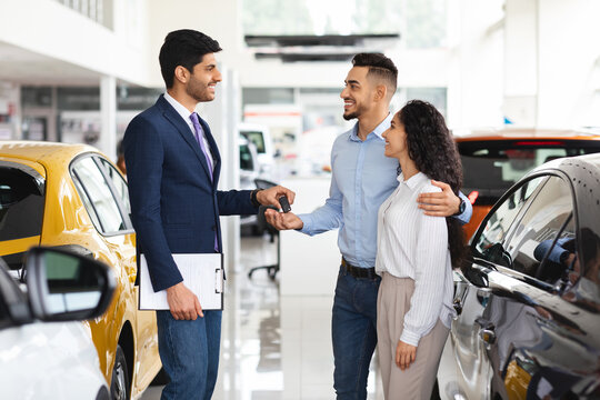 Cheerful sales associate giving arabic couple key from car
