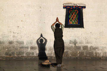 Person praying near a wall with a shadow in the Jokhang Temple in Lhasa, Tibet - obrazy, fototapety, plakaty