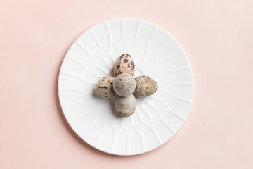 Minimal Easter image with quail eggs laid out as cross on white plate on pastel pink background.