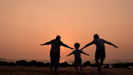 Silhouette of happy Asian family having fun and running on the beach at sunset, Playing in summer and freedom travel concept