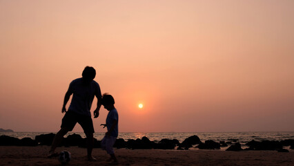 Fototapeta na wymiar Silhouette of Asian father and son playing football or soccer on the beach at sunset, Happy family trip in summer season