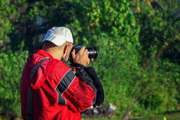 Side view of a young Caucasian male taking photo of the beautiful dense greenery in the forest