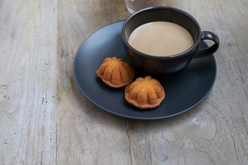 Selective focus on the Kuih Bahulu, a famous Malaysian cake on the black plate and a cup of coffee. Have a break concept. Noise, grain and grungy is visible on the subjects