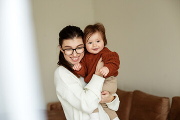 Young mother holds beautiful little daughter in arms. Mother and baby 8 months old play and laugh.