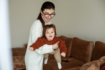 Young mother holds beautiful little daughter in arms. Mother and baby 8 months old play and laugh.