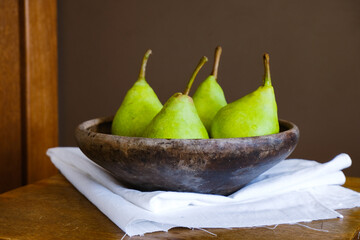 Green pears in a clay ancient old plate on a wooden table. Dark brown food template. Empty space. Food, ingredient, fall color, vitamin, fresh fruits, vegan organic produce, healthy nutrition, harvest
