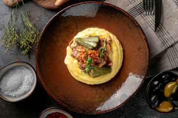 Mashed potatoes with beef stew in sauce, pickles and fried onions. Meat dish served on a plate, top view