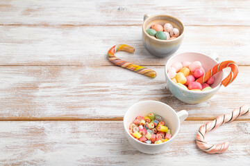 Heap of multicolored caramel candies in cups on white wooden background. copy space, side view.