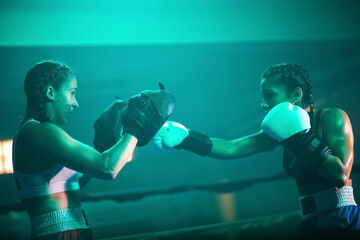 Side view of young boxer girls training in gloves on ring. Two sporty girls preparing for boxing match in dimly lit gym, improving punches and bout tactics. Extreme sport and healthy lifestyle concept