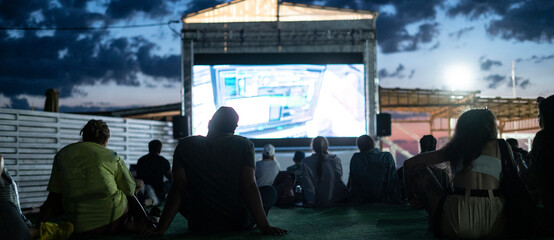 crowd of people watching a movie in the open air cinema at night