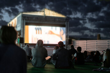 crowd of people watching a movie in the open air cinema at night