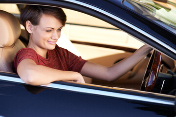 Enjoying a roadtrip in style. Shot of a beautiful young woman driving a luxury car.