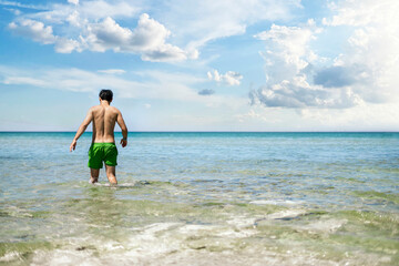 young man walking into the sea water to swim on a summer vacation