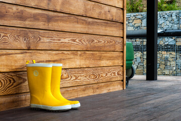 Children's yellow rubber boots stand on the terrace of a wooden house