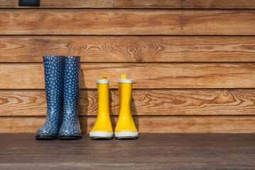 Blue and yellow rubber boots stand on the terrace. Adult and children's boots stand against the...