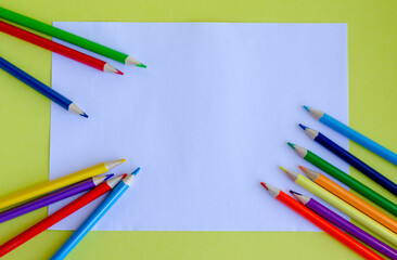 Multi-colored pencils and a white sheet of paper on a yellow background. The concept of creativity, development, learning