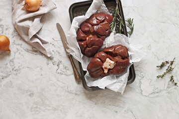 Raw beef kidneys ready to cook with vegetables and herbs on marble kitchen table. Flat layot, copy...