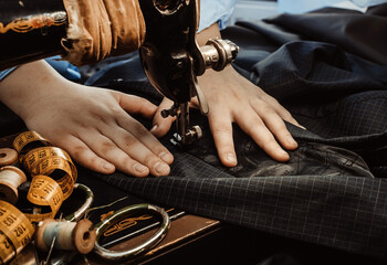 Tailor's hands close-up sew clothes on an old retro sewing machine. Tools for a tailor, fashion designer or seamstress
