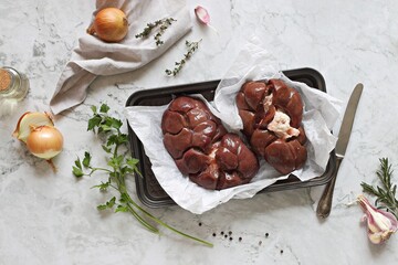 Raw beef kidneys ready to cook with vegetables and herbs on marble kitchen table. Flat layot, copy...