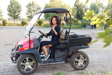 Cheerful young woman in black dress showing thumb up, poses in vehicle outside.