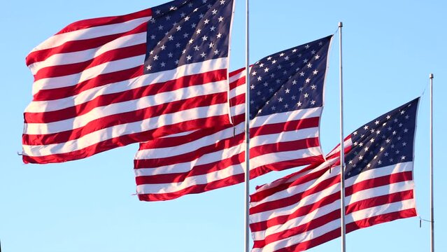 Three big American Flags, Old Glory, flying and rippling in morning sunlight, in graceful slow motion.