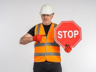 Builder orders to stop. Stop sign in hands of worker. Concept he warns of danger. Builder demonstrates stop sign. To metaphor of danger due to road works. Road worker on gray background.