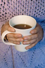 A cup of tea in the hands of a girl, close-up. Vertical photography.