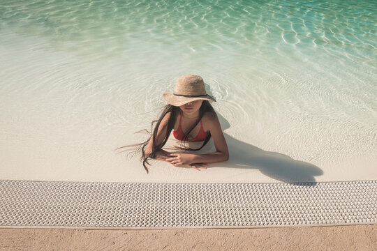 woman with hat and bikini relaxing in the swimming pool in summer
