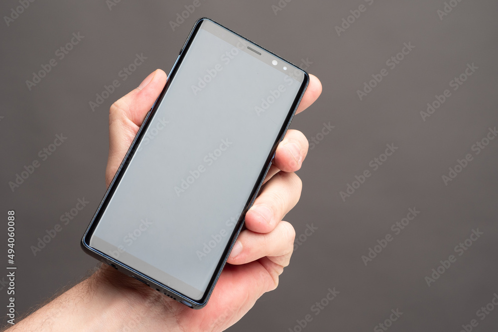 Poster phone in hand. smartphone with screen off. mobile phone on gray background. turned off cell phone cl