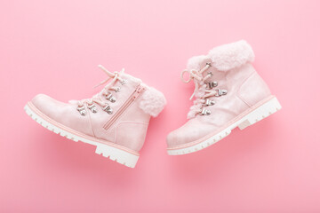 Leather warm child boots with fluffy fur, shoelaces and zipper on light pink floor background. Pastel color. Closeup. Top down view.
