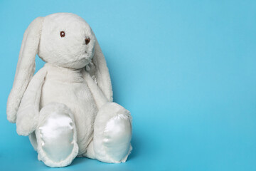 Stuffed bunny on blue background. Easter concept. Beaytiful white toy soft bunny sitting on colored...