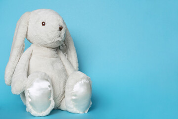 Stuffed bunny on blue background. Easter concept. Beaytiful white toy soft bunny sitting on colored background. Copy space for text