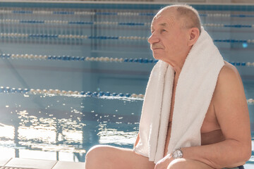 An elderly man with a white towel on his shoulders sits near fables on a bright, sunny day.