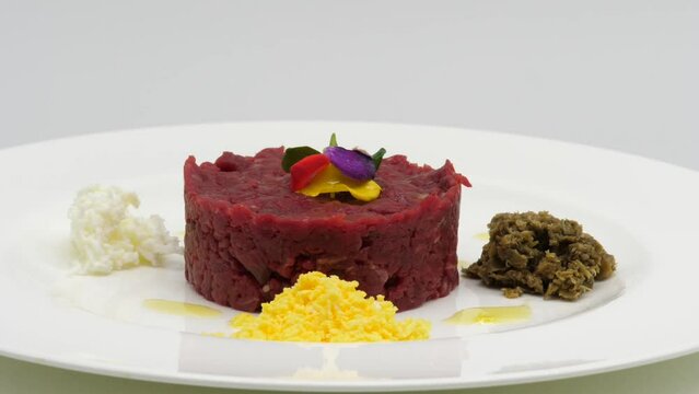 Tartare di Manzo servita su un piatto, con uovo e formaggio.
Piatto che gira per mostrare la composizione di tartare di Tonno.
