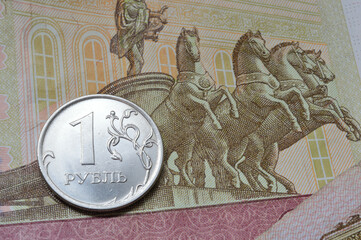Russian coin with a face value of 1 ruble lies on a banknote. Translation of the inscriptions on the coin: "1 ruble"
