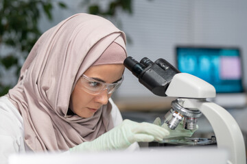 Young Muslim female researcher putting sample of bacteria on small glass while going to study it in...