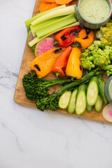 Grilled vegetables and crudite on wooden cutting board on white marble countertop
